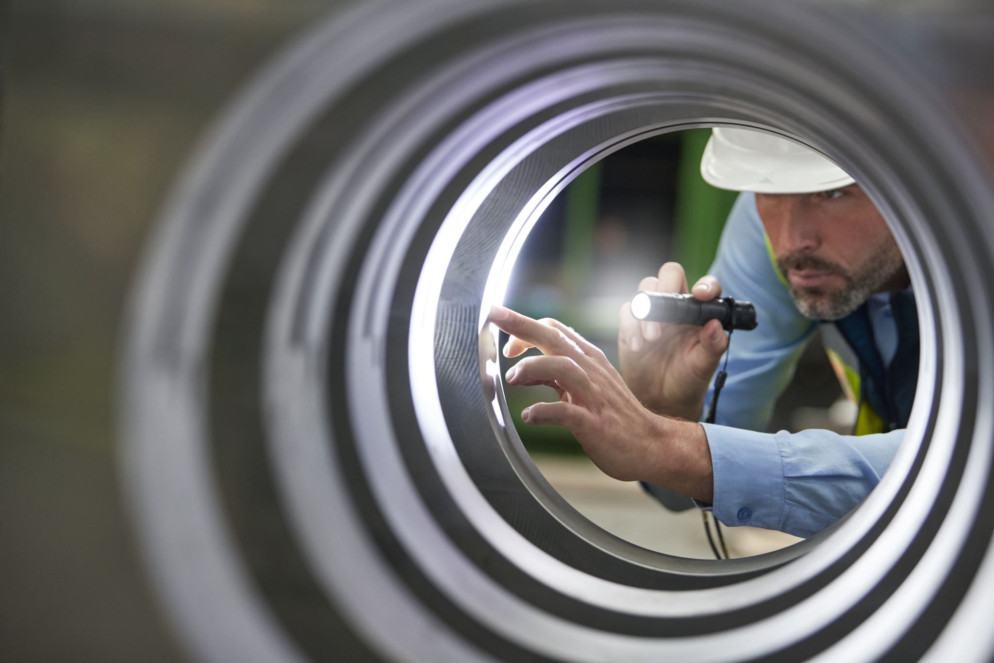 Male-engineer-with-flashlight-inspecting-steel-cylinder